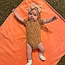 baby, infant, blanket, orange, headband, bow, carpet, socks, cute, smiling, arms_stretched, onesie, patterned_clothing, lying_down, indoor, child, person, soft_texture, floor, happy