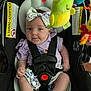 baby, car_seat, child, infant, toddler, bow, headband, toy, colorful, safety_harness, clothing, expression, indoor, cute, seat, child_safety, person, smile, face, closeup