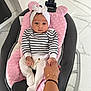 adult_hand, baby, baby_seat, child, comfort, cushion, cute, foot, footwear, headwrap, holding_hand, indoors, infant, knit_pants, marble_floor, modern_interior, person, pink_pillow, seated, striped_sweater