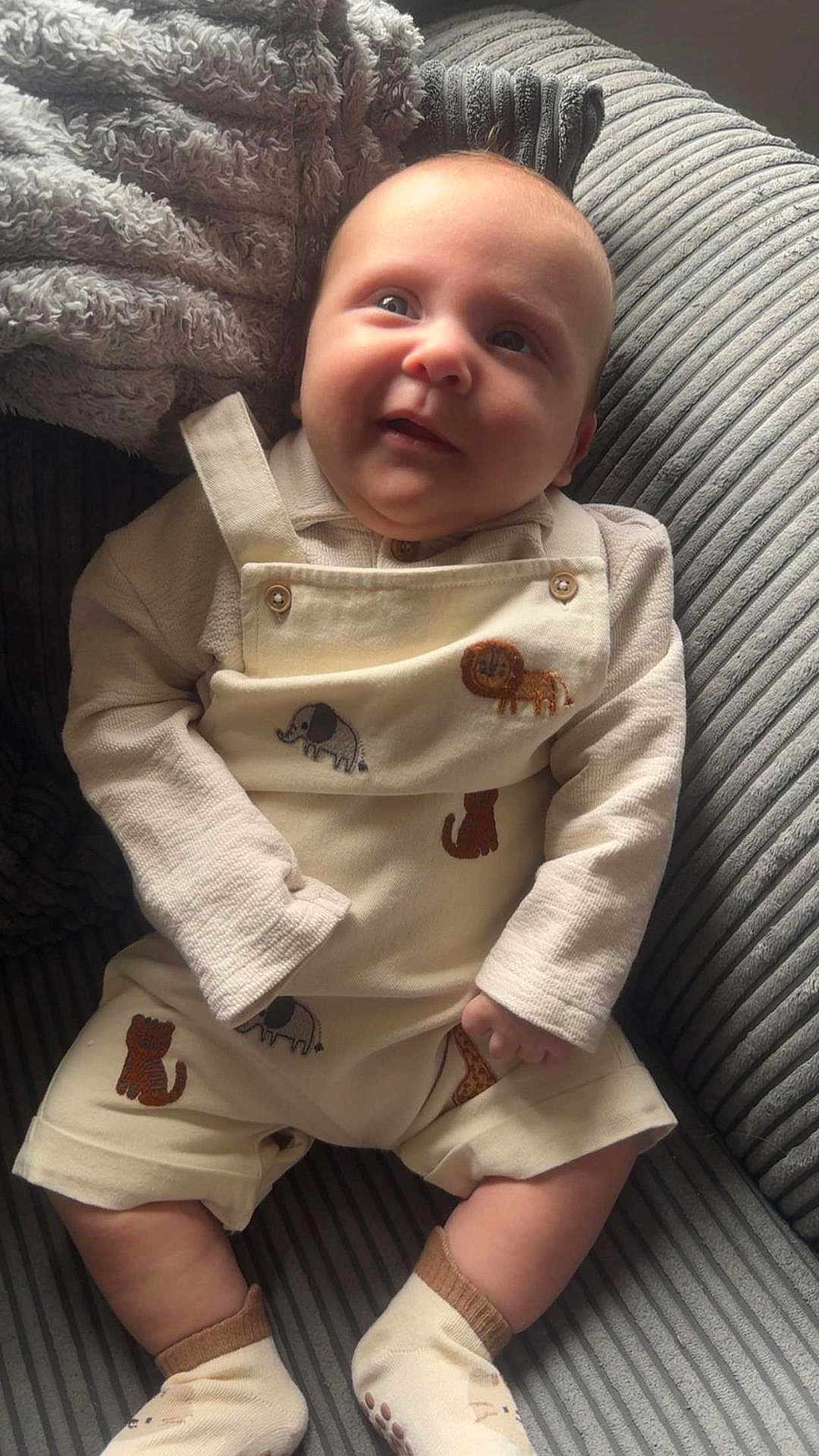 Micah joined the competition — help win amazing prizes! baby, child, infant, overalls, animal_patches, socks, cushion, chair, striped, soft_light, cute, smiling, cozy, indoors, portrait, person, clothing, fabric, texture, comfortable