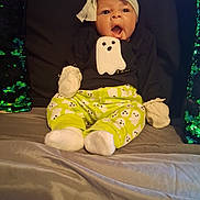Ma'Kenna is registered to the contest to win money with this photo: baby, child, infant, ghost_pattern, headwrap, mittens, socks, green, black_shirt, bed, pillow, sequin_pillow, surprised_expression, open_mouth, sitting, indoors, cute, comfortable, clothing, portrait