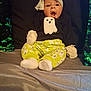 baby, child, infant, ghost_pattern, headwrap, mittens, socks, green, black_shirt, bed, pillow, sequin_pillow, surprised_expression, open_mouth, sitting, indoors, cute, comfortable, clothing, portrait