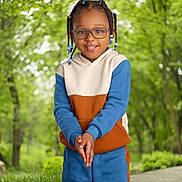 Nicholas is registered to the contest to win money with this photo: child, glasses, braids, beads, smile, hoodie, pants, outdoor, forest, trees, grass, pathway, nature, happy, person, portrait, casual_clothing, standing, daylight, greenery