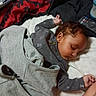 baby, sleeping, bed, blanket, clothing, remote_control, curly_hair, infant, pajamas, peaceful, child, indoors, rest, soft_light, portrait, person, cute, cozy, toddler, nap