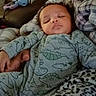baby, infant, sleeping, dinosaur_pajamas, blanket, hand, furniture, toy, couch, pattern, comfort, indoor, cozy, child, person, face, sleep, rest, cute, young