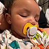 baby, sleeping, pacifier, onesie, dinosaur_pattern, close_up, infant, child, cute, peaceful, face, mouth, clothing, indoor, portrait, young, head, skin, hand, resting
