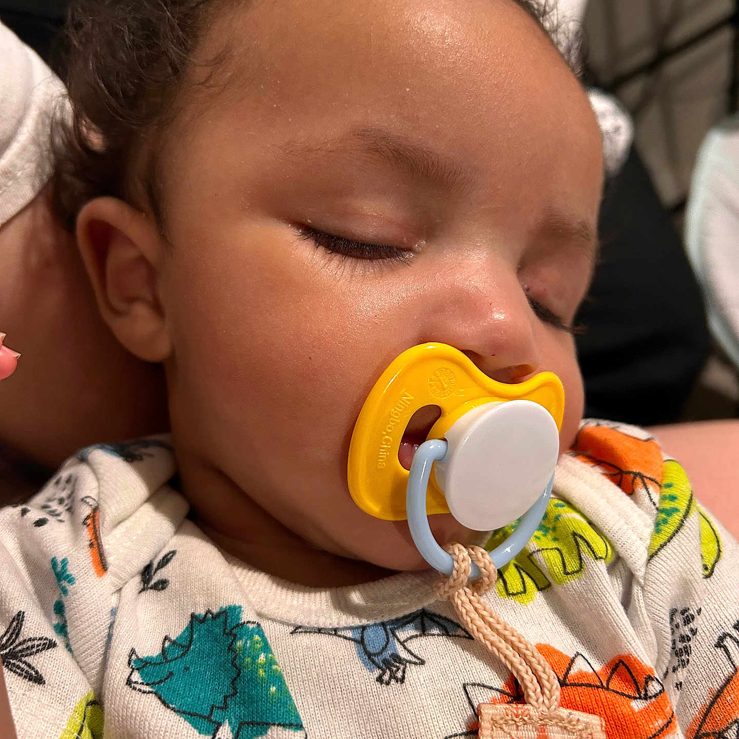 Davonta joined the competition — help win amazing prizes! baby, sleeping, pacifier, onesie, dinosaur_pattern, close_up, infant, child, cute, peaceful, face, mouth, clothing, indoor, portrait, young, head, skin, hand, resting