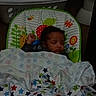 baby, sleeping, blanket, baby_seat, indoor, laundry_basket, toilet, patterned_blanket, colorful, child, nursery, resting, cozy, infant, face, curly_hair, comfort, peaceful, furniture, home