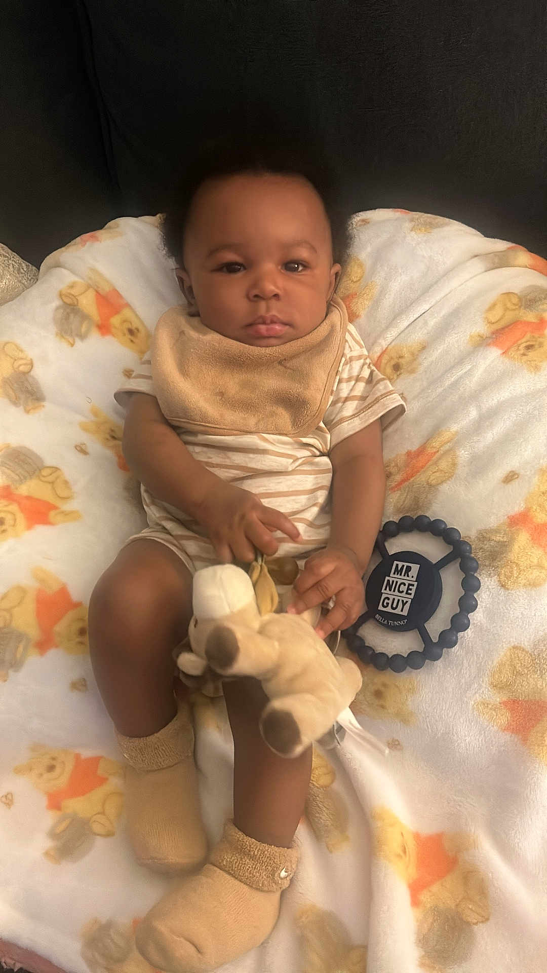 Messiah is registered to the contest to win money with this photo: baby, infant, plush_toy, blanket, teddy_bear_print, bib, socks, striped_clothing, toy, child, indoor, soft_texture, cute, calm, seated, person, cozy, nursery, young_child, comfort