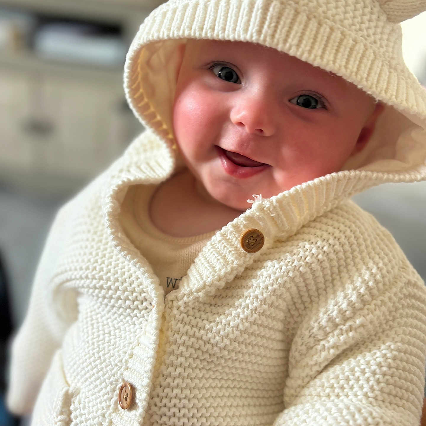 Mali is registered to the contest to win money with this photo: apparel, baby, button, child, closeup, cute, face, happy, hood, indoors, infant, knitted_clothing, person, portrait, smile, soft_light, sweater, warm, white, young