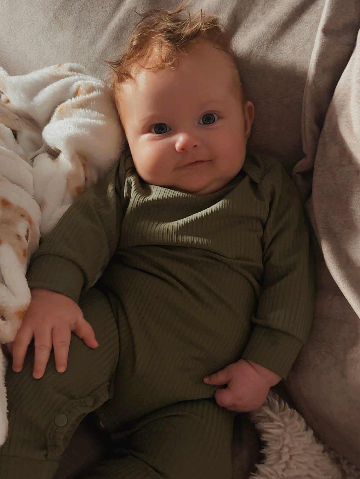 Enzo is registered to the contest to win money with this photo: baby, infant, child, face, smile, curly_hair, green_clothing, onesie, couch, blanket, soft_texture, relaxed, indoors, cute, portrait, hand, fingers, comfortable, warm, cozy