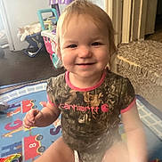 Nova is registered to the contest to win money with this photo: toddler, child, smiling, indoor, play_mat, toy, cat, couch, carhartt, camouflage, person, happy, sitting, furniture, floor, carpet, light, hair, cute, baby
