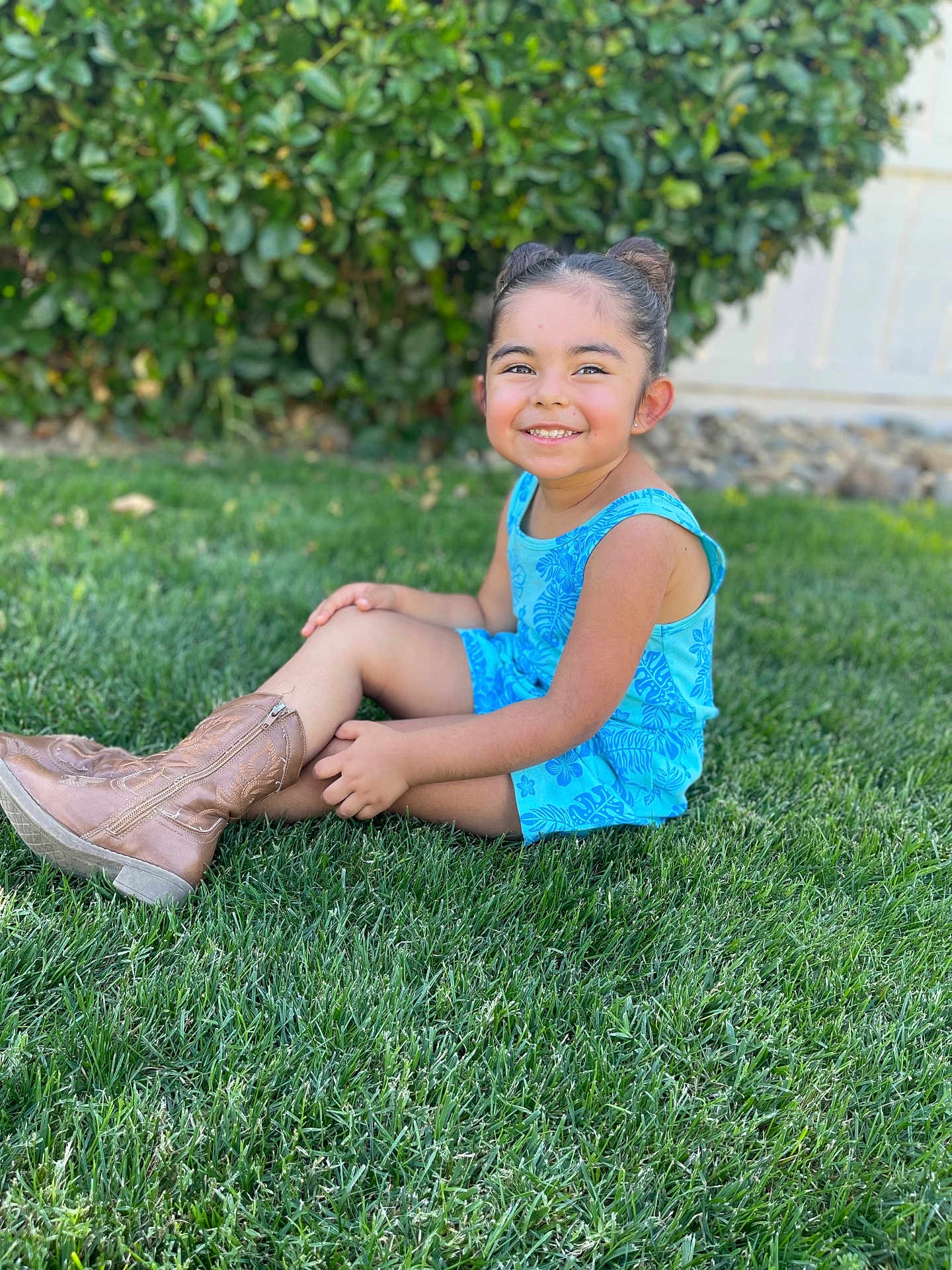 Ariana joined the competition — help win amazing prizes! child, girl, smiling, grass, greenery, outdoor, blue_clothing, boots, hair_buns, romper, nature, sunlight, happy, portrait, sitting, fence, hedge, casual, daytime, cute