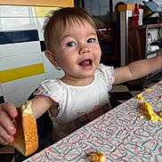 Emily joined the competition — help win amazing prizes! toddler, child, bread, food, table, smile, happy, mealtime, diner, scrambled_eggs, crumbs, white_shirt, indoor, person, face, cute, expression, colorful, highchair, eating