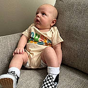 Kacey joined the competition — help win amazing prizes! baby, infant, child, onesie, socks, shoes, checkered, couch, furniture, indoor, curious, cute, chubby, person, apparel, seated, head, face, skin, casual