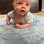 Kacey is registered to the contest to win money with this photo: baby, infant, blue_blanket, carpet, indoor, furniture, wooden_dresser, curious, arms, face, eyes, short_sleeve_shirt, green_shorts, closeup, child, person, crawling, floor, soft_texture, home