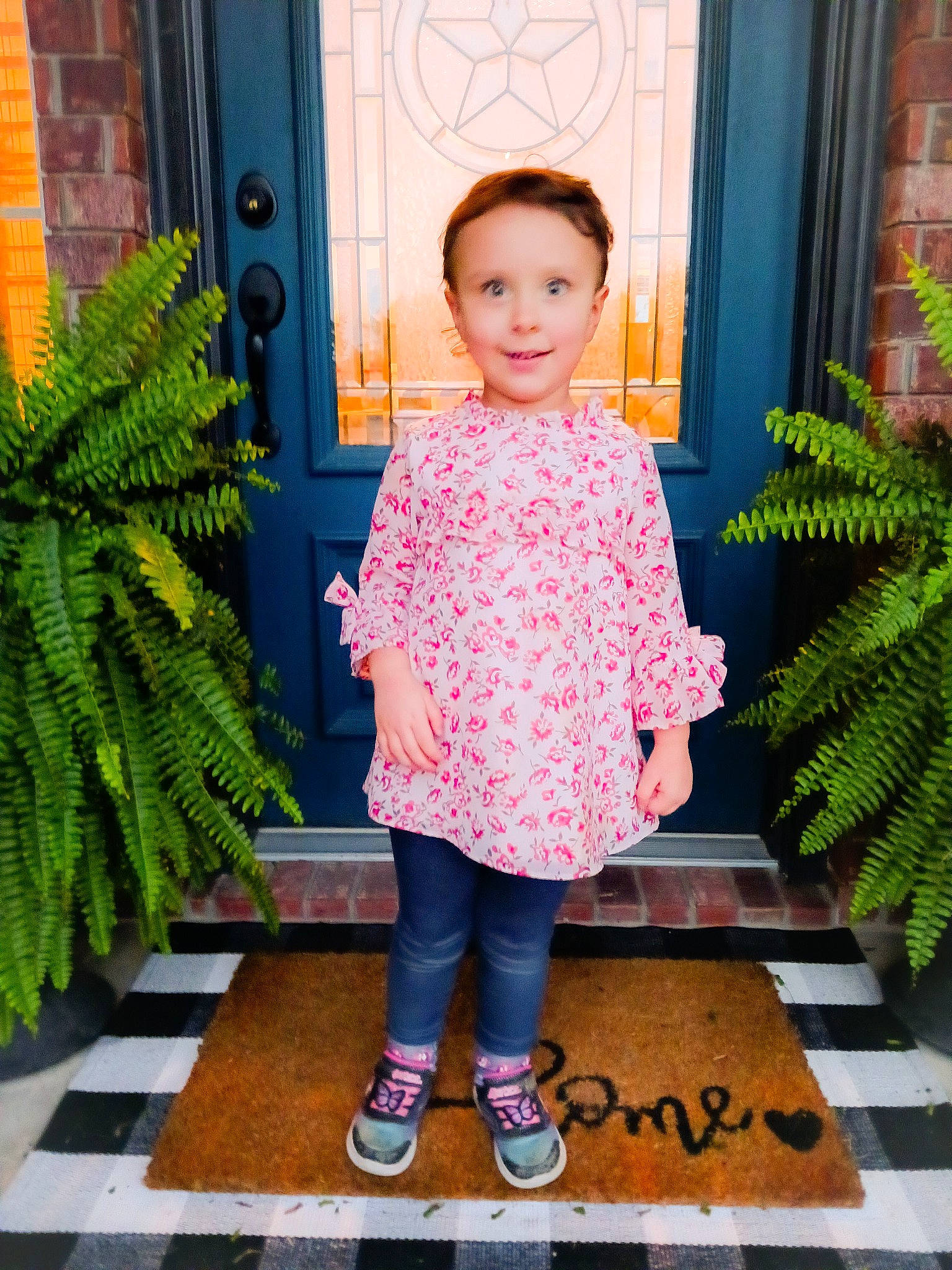 Isabella is registered to the contest to win money with this photo: baby_toddler_clothing, child, door, flooring, flowerpot, green, houseplant, joy, magenta, pattern, person, photograph, pink, plant, sleeve, smile, snapshot, standing, terrestrial_plant, textile