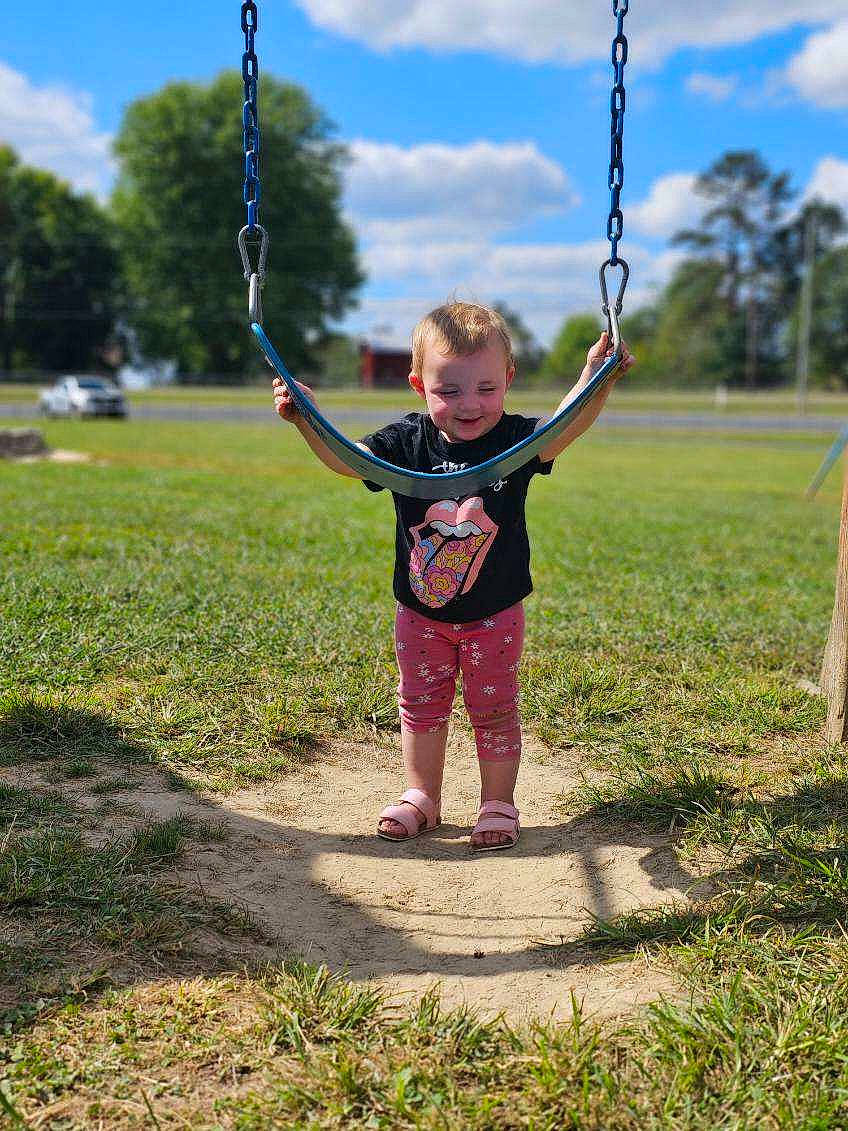 Ella is registered to the contest to win money with this photo: child, cloud, gesture, grass, happy, joy, leisure, nature, people_in_nature, person, plant, playground, public_space, recreation, sky, smile, standing, summer, swing, toddler