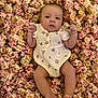baby, infant, flower_bed, floral_pattern, romper, pink_flowers, cream_flowers, skin, cute, lying_down, small_fists, head, legs, feet, soft_lighting, portrait, close_up, natural_colors, outdoor, adorable