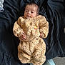 baby, infant, teddy_bear_outfit, clothing, blanket, bed, face, person, sleepy, cute, cozy, hand, footwear, lying_down, indoor, soft_texture, warm, child, newborn, portrait