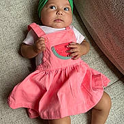 Peyton joined the competition — help win amazing prizes! baby, child, infant, person, face, headband, bow, pink_dress, watermelon_patch, couch, furniture, skin, hand, leg, foot, sitting, indoors, textile, clothing, cute