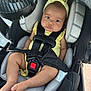 baby, car_seat, child, yellow_clothing, headband, fan, straps, seatbelt, infant, cute, indoors, sitting, person, chubby_cheeks, foot, legs, black_straps, gray_cushion, car_interior, secure