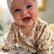 Estrella is registered to the contest to win money with this photo: baby, smiling, face, headband, bow, eyes, sweater, patterned_clothing, infant, cute, happy, portrait, child, indoors, blanket, hand, closeup, cheerful, soft_light, young
