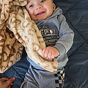 Antonio is registered to the contest to win money with this photo: baby, child, smile, blanket, hand, clothing, quilt, blue, grey, happy, infant, toddler, face, cute, soft, pattern, indoor, person, holding, cozy