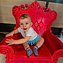 baby, child, smiling, red_chair, indoor, cute, sitting, happy, playful, person, shorts, white_shirt, socks, furniture, decorative_chair, expression, young_child, portrait, hands, eyes