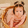 adorable, baby, baby_girl, basket, bracelet, child, cozy, cute, floor, hair_ties, home, indoor, infant, knitted_blanket, looking_up, pink_dress, pony_tails, portrait, soft_lighting, woven_basket