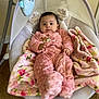 baby, pink_onesie, blanket, baby_swing, toys, floral_pattern, carpet, indoor, child, cute, infant, comfort, relaxing, plush, smiling, face, person, warm, soft, home