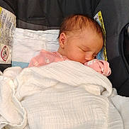 Lydia is registered to the contest to win money with this photo: newborn, baby, sleeping, blanket, pink_clothing, car_seat, face, infant, rest, cozy, child, young, warning_label, fabric, head, peaceful, soft, wrapped, indoors, portrait