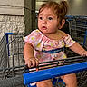 Remi joined the competition — help win amazing prizes! toddler, child, shopping_cart, walmart, blue_eyes, pink_dress, floral_pattern, hair_tied, earrings, supermarket, indoor, grip, curious, seatbelt, metal, shopping, retail, aisle, store, person