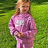 child, girl, toddler, portrait, outdoor, garden, grass, sunlight, pink_clothing, hoodie, tracksuit, sportswear, nike, sneakers_absent, long_hair, hair_clip, smiling, standing, playground_absent, nature