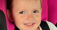 Savannah is registered to the contest to win money with this photo: child, toddler, smiling, happy, portrait, car, car_seat, seatbelt, harness, pink, hair_buns, brown_hair, white_shirt, face, teeth, indoors, vehicle, passenger, road_trip, photography