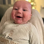 Noah-James is registered to the contest to win money with this photo: baby, smiling, face, infant, clothing, striped_outfit, text_on_clothing, person, portrait, happy, cozy, indoor, soft_light, blurred_background, warm_colors, newborn, cute, expression, closeup, child