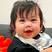 Yohan is registered to the contest to win money with this photo: baby, child, smiling, face, hair, bib, clothing, indoor, portrait, cute, happy, person, skin, eyes, mouth, hand, furniture, plush_toy, black_shirt, toddler