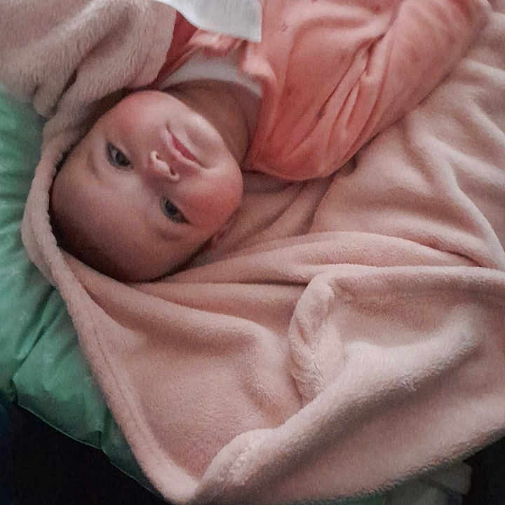 Inaya participe au concours pour gagner de l'argent avec cette photo : baby, blanket, pink, child, face, lying_down, cushion, indoor, soft_texture, infant, clothing, portrait, messaging_app, screenshot, cozy, young_child, looking, wrapped, cute, resting