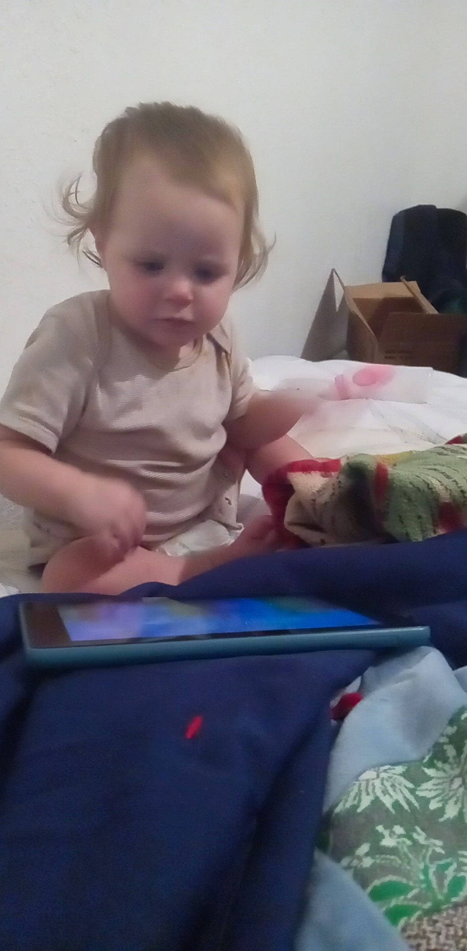 Ernestine is registered to the contest to win money with this photo: baby, baby_toddler_clothing, bed, bedding, cheek, child, comfort, electric_blue, electronic_device, finger, fun, hair, linens, person, play, room, sitting, sleeve, t_shirt, toddler