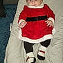 baby, infant, red_dress, headband, bow, socks, blanket, cushion, indoor, carpet, smiling, person, child, cute, holiday, christmas_outfit, lying_down, clothing, face, footwear
