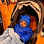 baby, child, stroller, blue_jacket, blanket, indoor, shopping, floor, wood_floor, clothing, hat, face, cute, warm, bundle, person, infant, coat, hood, toy