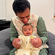 Neev joined the competition — help win amazing prizes! baby, man, smile, happy, indoor, traditional_clothing, holding_hands, bed, blanket, portrait, person, infant, family, seated, cute, love, toddler, casual, head, clothing