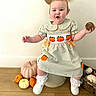 Paisley joined the competition — help win amazing prizes! baby, child, infant, smiling, happy, portrait, pumpkin, autumn, fall, dress, bow, gourd, holding_object, sitting, white_shoes, socks, indoor, home_decor, wooden_floor, seasonal_decoration