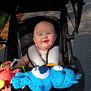 Paisley is registered to the contest to win money with this photo: baby, babytrend, blue_eyes, child, clothing, cute, daylight, face, happy, head, infant, outdoor, person, plush_toy, road, seatbelt, smiling, stroller, sunlight, toy