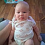 Paisley joined the competition — help win amazing prizes! baby, child, infant, tongue_out, sitting, person, floor, playmat, toy, wooden_floor, clothing, onesie, arm, hand, indoor, cute, smiling, skin, head, legs