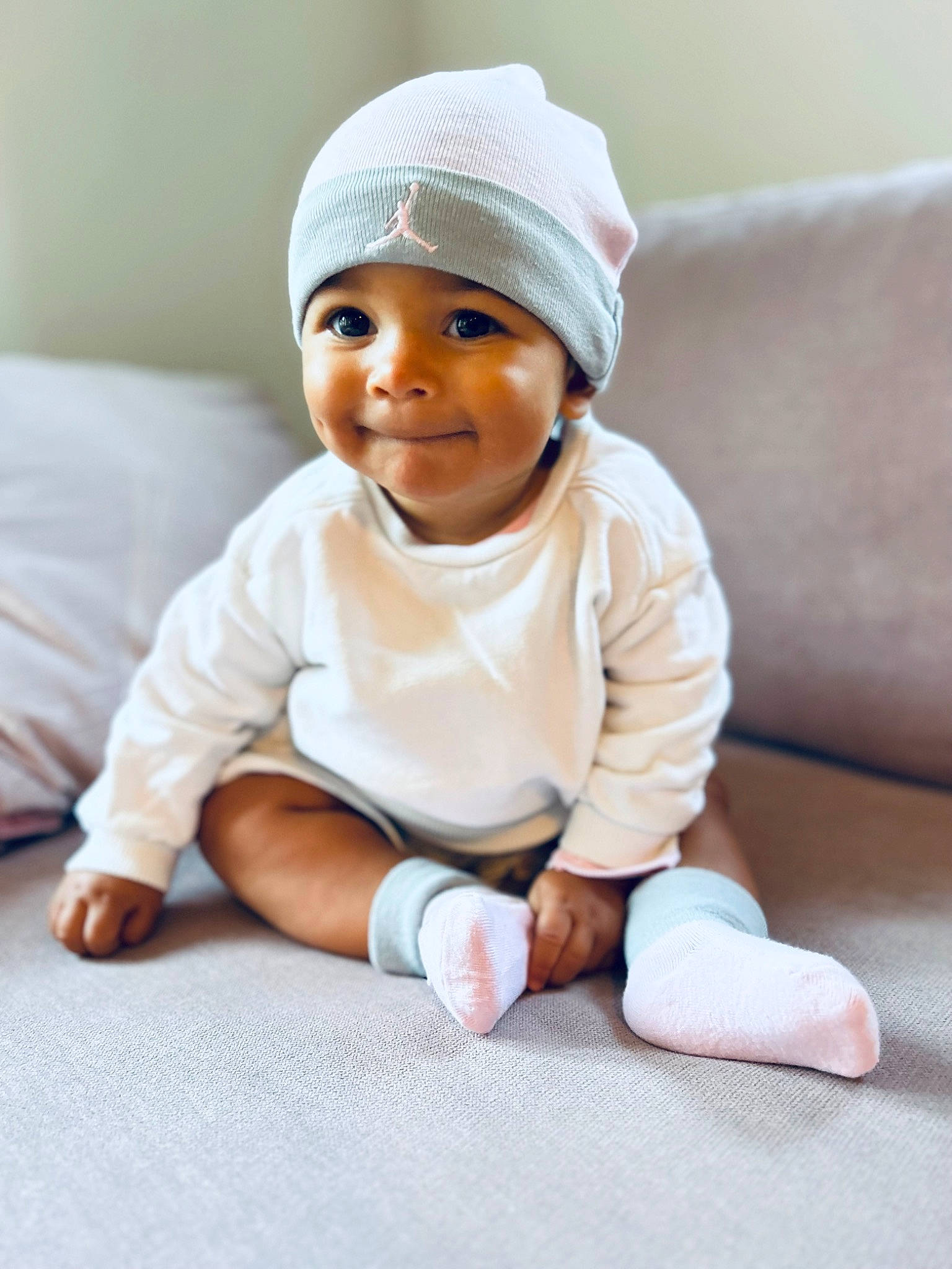 Maddy participe au concours pour gagner de l'argent avec cette photo : baby, baby_toddler_clothing, barefoot, beanie, cap, cheek, child, comfort, facial_expression, flooring, happy, headwear, joy, knit_cap, linens, person, portrait_photography, room, sitting, skin