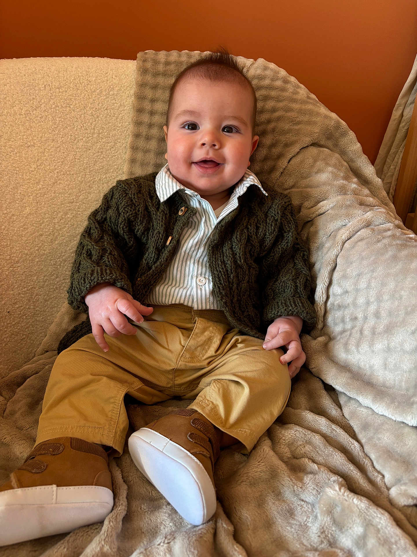 Jules a rejoint le concours — aidez-le/la à gagner de superbes lots ! baby, child, smile, clothing, pants, shoes, cardigan, blanket, couch, face, person, indoors, furniture, happy, cute, portrait, seated, warm_colors, cozy, young_child