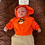 Elio participe au concours pour gagner de l'argent avec cette photo : baby, child, hoodie, orange_hoodie, winnie_the_pooh, cartoon_print, sign, brown_blanket, beige_pants, infant, lying_down, cute, one_month, soft_texture, indoors, clothing, person, portrait, baby_clothes, face