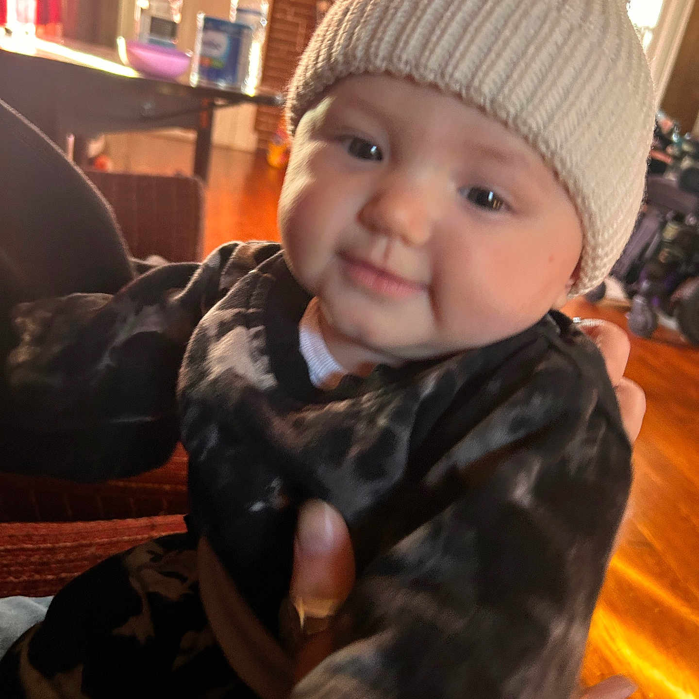 Khamiya joined the competition — help win amazing prizes! baby, black_clothing, blurred_background, bottle, child, cozy, face, furniture, hand, hat, indoor, knit_hat, person, pom_pom, portrait, smile, sweater, table, warm_light, wooden_floor