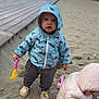 Thélyo participe au concours pour gagner de l'argent avec cette photo : child, toddler, sand, beach, jacket, hood, toy, bucket, rake, playground, outdoor, clothing, footwear, sand_toys, wooden_boardwalk, sky, clouds, playing, curious, winter_wear